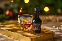 A miniature bottle of Tia Mari beside a small glass with ice in it against a festive background WIDE