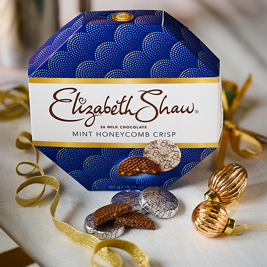 A blue Hexagonal box with gold ribbon at the side, and some chocolate mints at the front