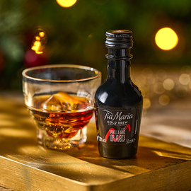 A miniature bottle of Tia Mari beside a small glass with ice in it against a festive background