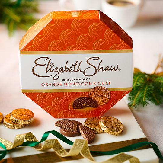 A hexagon orange box with chocolate mints at the front against a festive background
