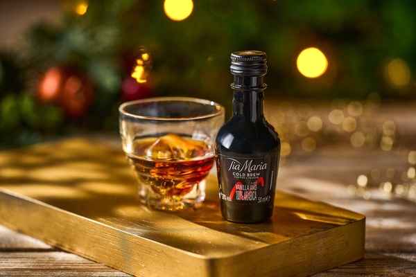 A miniature bottle of Tia Mari beside a small glass with ice in it against a festive background WIDE